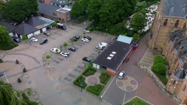 Park yeri, güneş panelli bir bina, manzaralı dairesel plaza, çevresindeki yamaç yapıları ve yayalar ile büyük bir kilisenin yanındaki bir kasaba meydanının havadan görüntüsü..