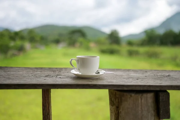 Cup of coffee on a wooden table over mountains landscape and rice field with sunlight. Beauty nature background.