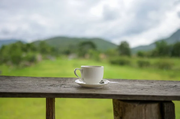Cup of coffee on a wooden table over mountains landscape and rice field with sunlight. Beauty nature background.
