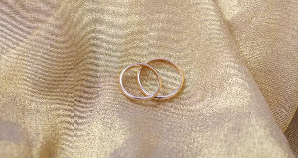 A pair of golden wedding rings on golden background