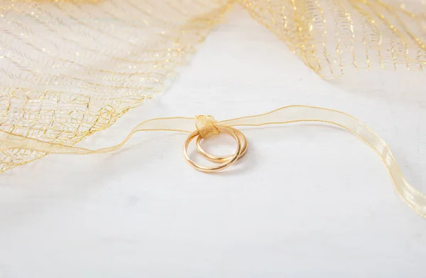 A pair of golden wedding rings tied with a golden ribbon on white wooden background, copy space