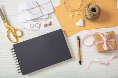 Düğün hazırlığı. Siyah defter ve düğün davetiyeleri bir beyaz tahta masa, kopya alanı üzerinde düz lay ve en iyi görünümü.