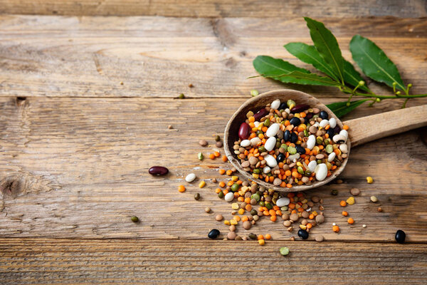 Healthy diet concept. Assortment of legumes in a ladle and spilled on a wooden tabletop background, copy space.