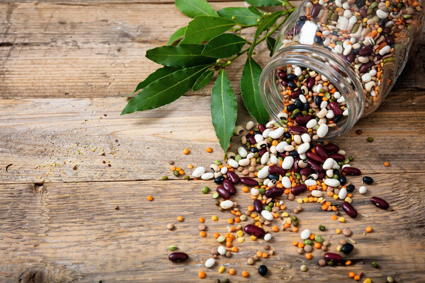 Healthy diet concept. Assortment of legumes in a glass jar and spilled on a wooden tabletop background, copy space.