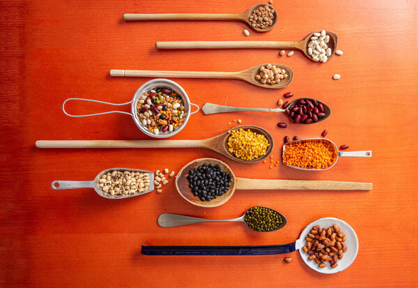 Healthy diet concept.Top view of fflat lay of assortment of legumes on orange tabletop background, in scoop and ladles.