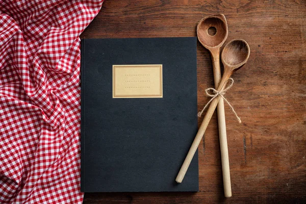Cooking recipes book. Notebook, kitchen utensils and red tablecloth on wooden table, top view