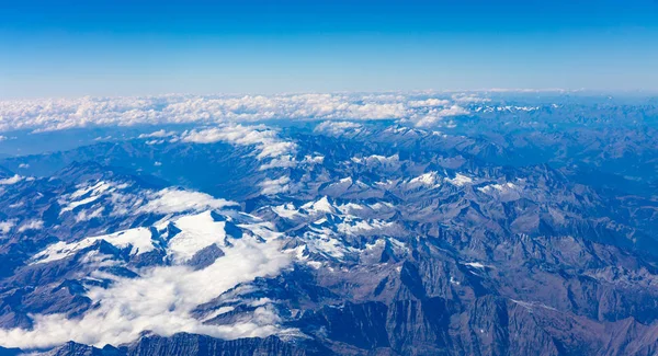 Mountains with snow and blue sky. Aerial view out of a plane window.