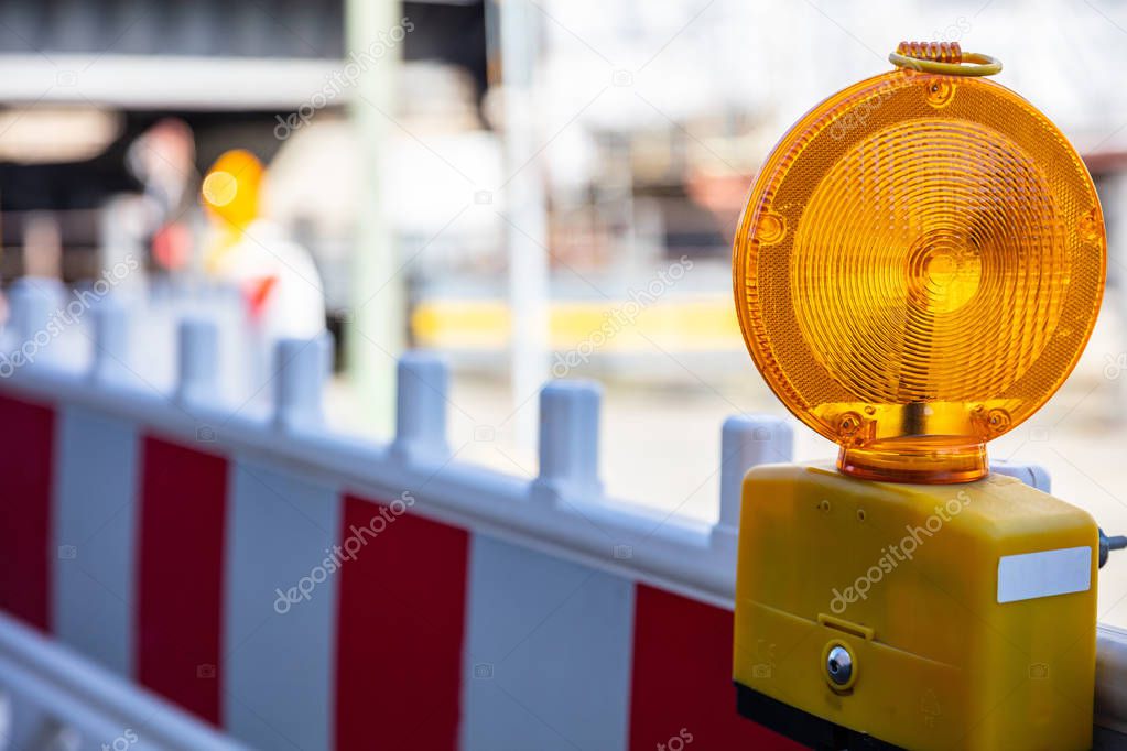 Construction site and safety. Street barricade with warning signal lamp on a road, blur site background