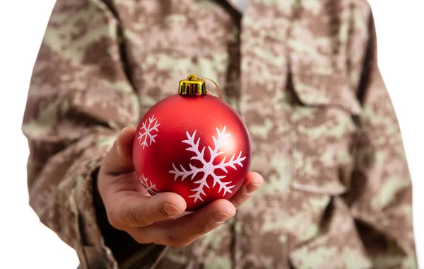 クリスマスと軍 赤いクリスマス ボール立っている白い背景の上に保持している若い兵士 — ストック写真