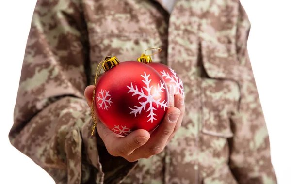 クリスマスと軍 赤いクリスマス ボール立っている白い背景の上に保持している若い兵士 — ストック写真