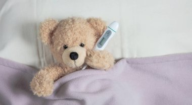 Ateş, soğuk, baca kavramı. Sevimli teddy yatakta bir termometre tutarak sıcak bir battaniye ile örtülü