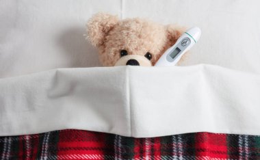 Ateş, soğuk, baca kavramı. Sevimli teddy yatakta sıcak bir battaniye ile örtülü bir termometre ile