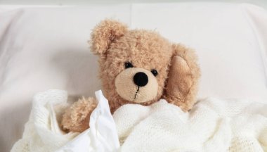 Soğuk, baca veya anti kavramı. Sevimli teddy yatakta bir doku tutarak sıcak bir battaniye ile örtülü