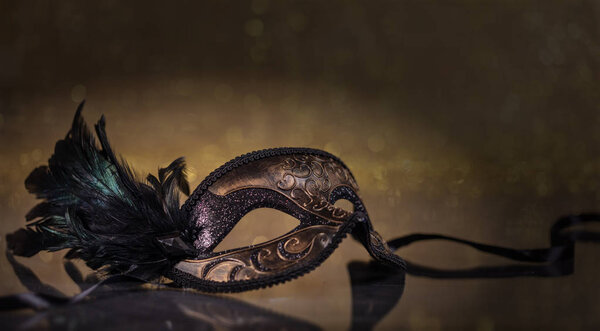 Время карнавала. Венецианская маска с перьями на темно-золотом фоне, отражения, копировальное пространство
