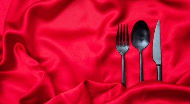 Sevgililer günü akşam yemeği, tablo, yer. Çatal bıçak takımı, siyah çatal, kaşık ve bıçak kopya alanı, kırmızı saten arka plan üzerinde görünümü top.