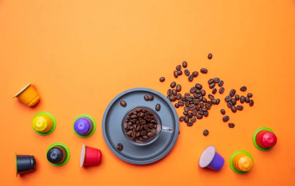 Coffee cup, beans and capsules, pods, on bright orange color background, copy space, top view