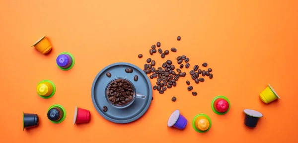 Coffee cup, beans and capsules, pods, on bright orange color background, copy space, top view