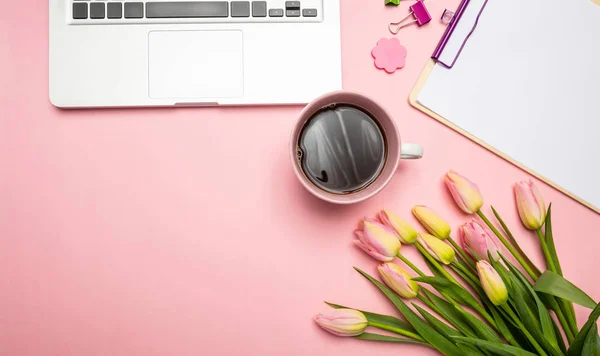 Womens, mothers day concept. Pink tulips bouquet and computer laptop on pink pastel background, top view, copy space