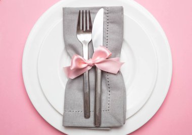 Pembe tablo yer ayarını. Pembe renkli arka plan, closeup üstten görünüm üzerinde şerit ve beyaz plakalı gri kumaş peçete,