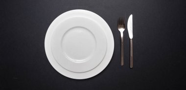 Yer sofra siyah. Dizi boş beyaz tabak ve çatal bıçak takımı siyah renk arka plan, üstten görünüm, kopya alanı