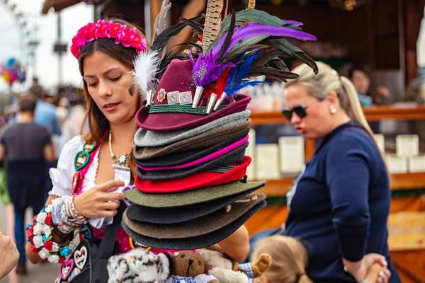 München, Tyskland, Oktoberfest, ung vacker kvinna i Folkdräkt håller en stack av tyrolska alpin hattar — Stockfoto