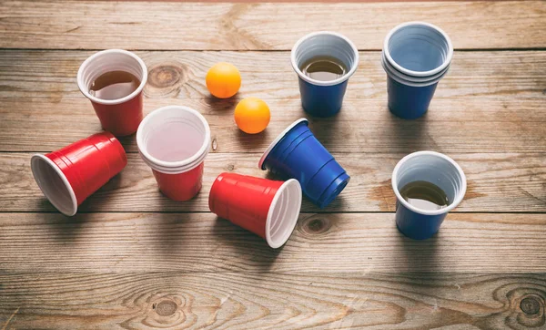 Beer pong. Kelímky plastové červené a modré barvy a ping pong míčky na dřevo — Stock fotografie