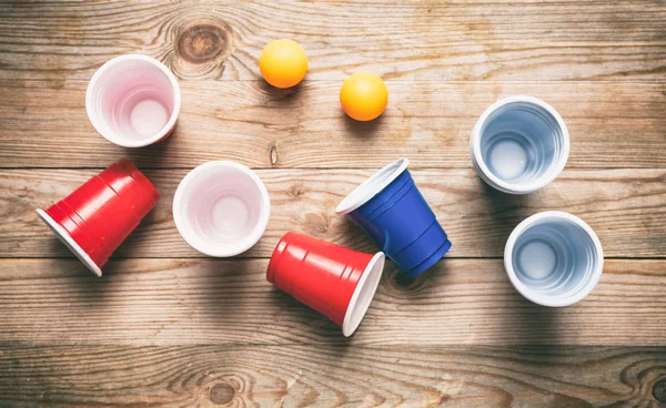 Cerveja-pongue. Copos de plástico de cor vermelha e azul e bolas de ping pong na madeira, vista superior — Fotografia de Stock