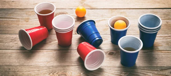 Beer pong. Plastic red and blue color cups and ping pong balls on wood