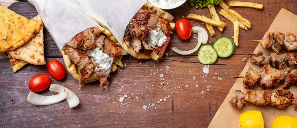 Gyro pita, shawarma, souvlaki. Deux enveloppements de pain pita et des brochettes de viande sur une table en bois — Photo