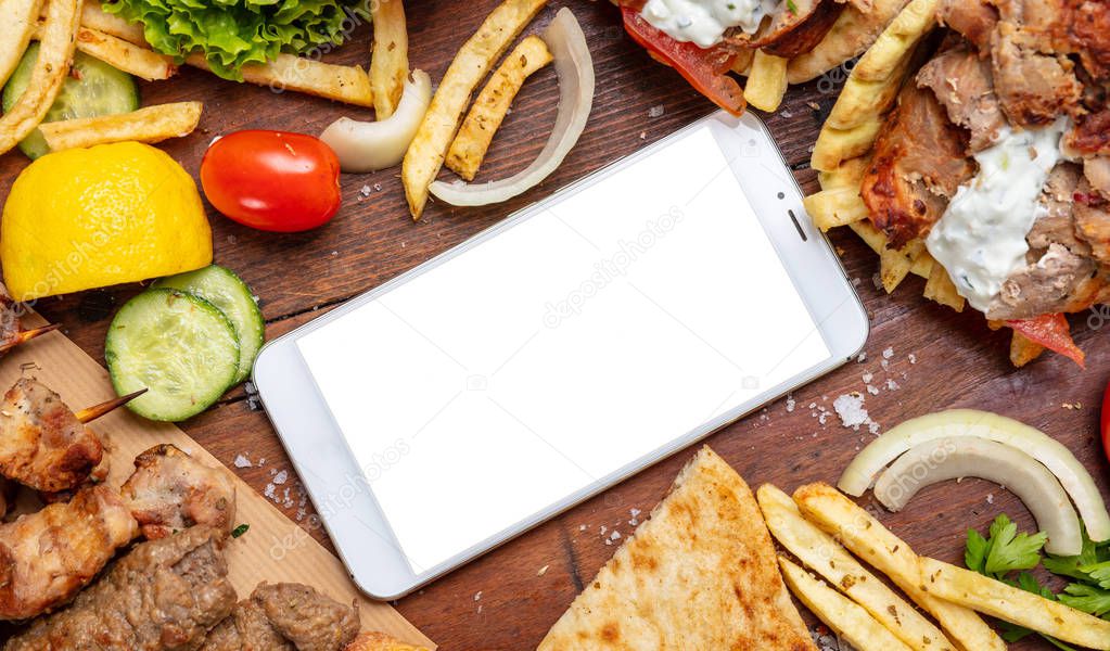 Gyro pita, shawarma, online order. Two wraps with meat, and blank screen mobile phone on wooden table