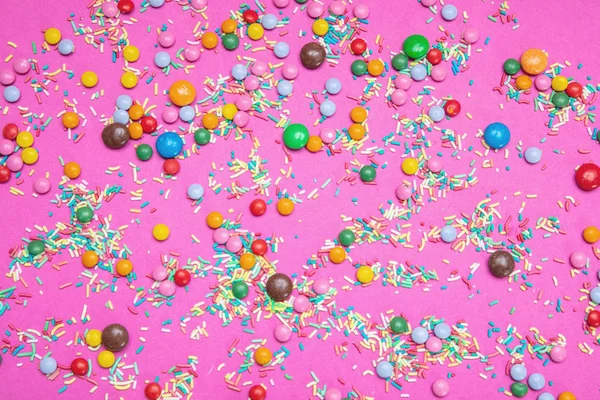 Концепция дня рождения. Красочные брызги и конфеты на ярко-розовом фоне — стоковое фото