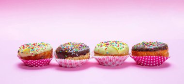 Pembe arka planda buzlanma ve renkli Sprinkles ile mini kekler