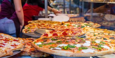 Bir dükkan vitrininde İtalyan pizza çeşitleri. Pizza servisi yapan kadın işçiler.