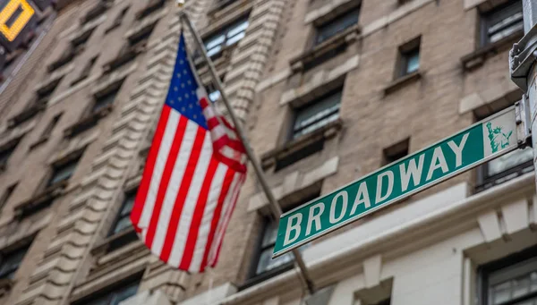 Broadway yol tabelası. Blur Amerikan bayrağı ve binalar cephe arka plan, Manhattan şehir — Stok fotoğraf