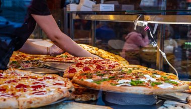 Bir dükkan vitrininde İtalyan pizza çeşitleri. Kadın işçi hizmet