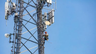 İletişim bakımı. Teknisyen mavi gökyüzü arka plan karşı telekom kulesinde tırmanma