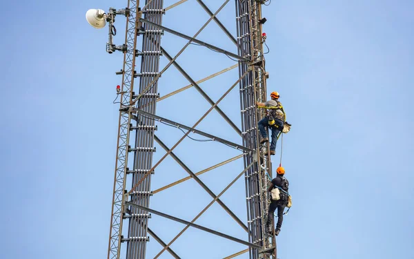 电信维护。两名修理工在蓝天背景上攀爬塔楼 — 图库照片