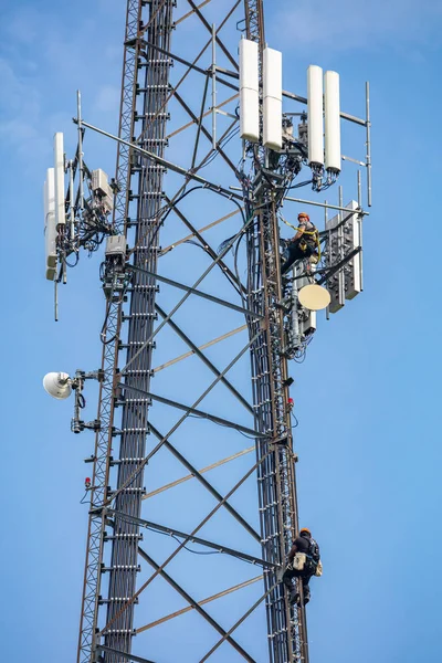 Коммуникационное обслуживание. Техник взбирается на телекоммуникационную вышку на фоне голубого неба — стоковое фото