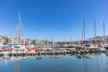 Marina Zeas Pire, Yunanistan. Birçok demirli tekne. Teknelerin yansıması, mavi sakin deniz, şehir ve gökyüzü arka plan