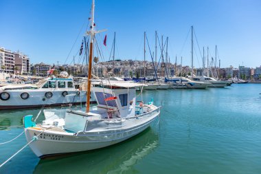 Marina Zeas Pire, Yunanistan. Beyaz demirli balıkçı teknesi ve direkli yatlar. Mavi sakin deniz, şehir ve gökyüzü arka plan.