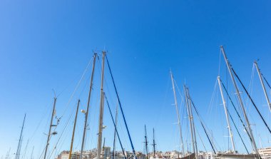 Yatlar Marina Zeas, Yunanistan'da berrak mavi gökyüzüne karşı üstleri direnir. Halatlı dikey çizgiler, şehir arka planı