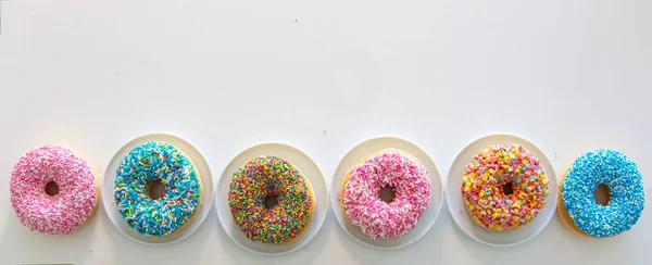 Donuts mit farbenfroher Dekoration auf weißem Hintergrund. Ansicht von oben — Stockfoto