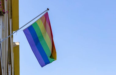 Eşcinsel gurur bayrağı açık mavi gökyüzüne karşı sallayarak