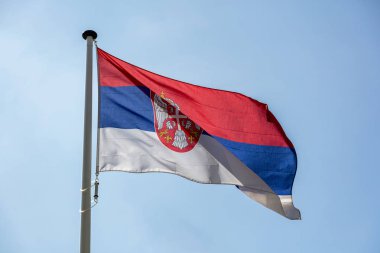 Açık mavi gökyüzüne karşı sallanan Sırp bayrağı