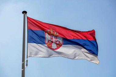 Açık mavi gökyüzüne karşı sallanan Sırp bayrağı