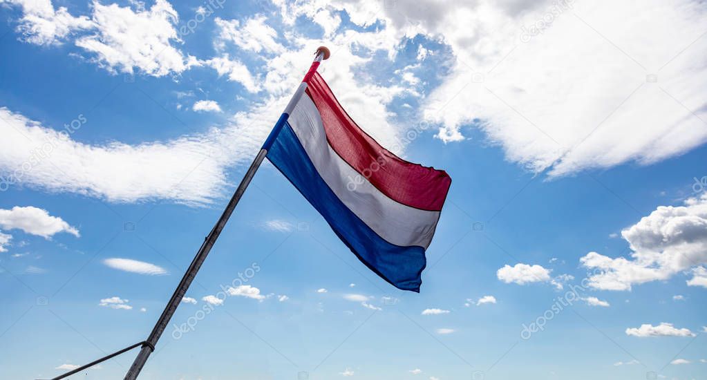 Holland flag waving against blue sky with clouds