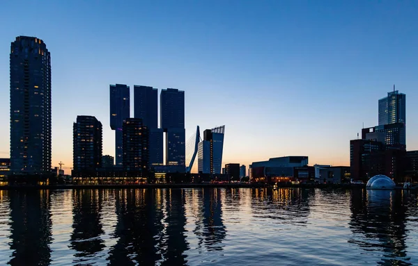 Rotterdam ciudad Países Bajos rascacielos iluminados, reflejos sobre el agua, la hora de la puesta del sol, cielo azul claro —  Fotos de Stock