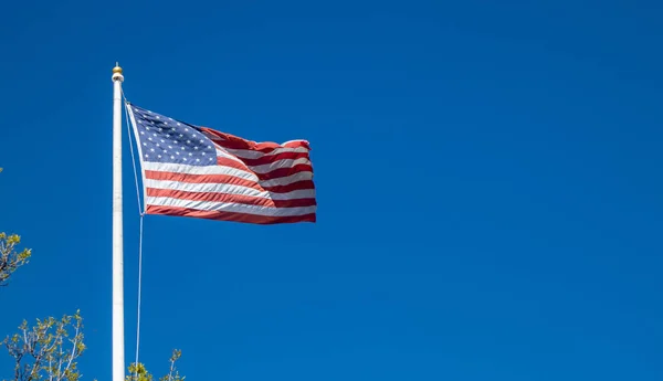 Flagge der Vereinigten Staaten auf einer Stange, die vor blauem Himmel weht. — Stockfoto