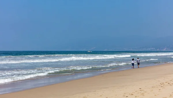 Fiatal pár sétált a homokos tengerparton. Kék óceán tenger hullámai, tiszta kék ég egy napsütéses tavaszi napon — Stock Fotó