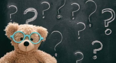Bir soru işareti ile tahtaya karşı gözlük giyen sevimli oyuncak